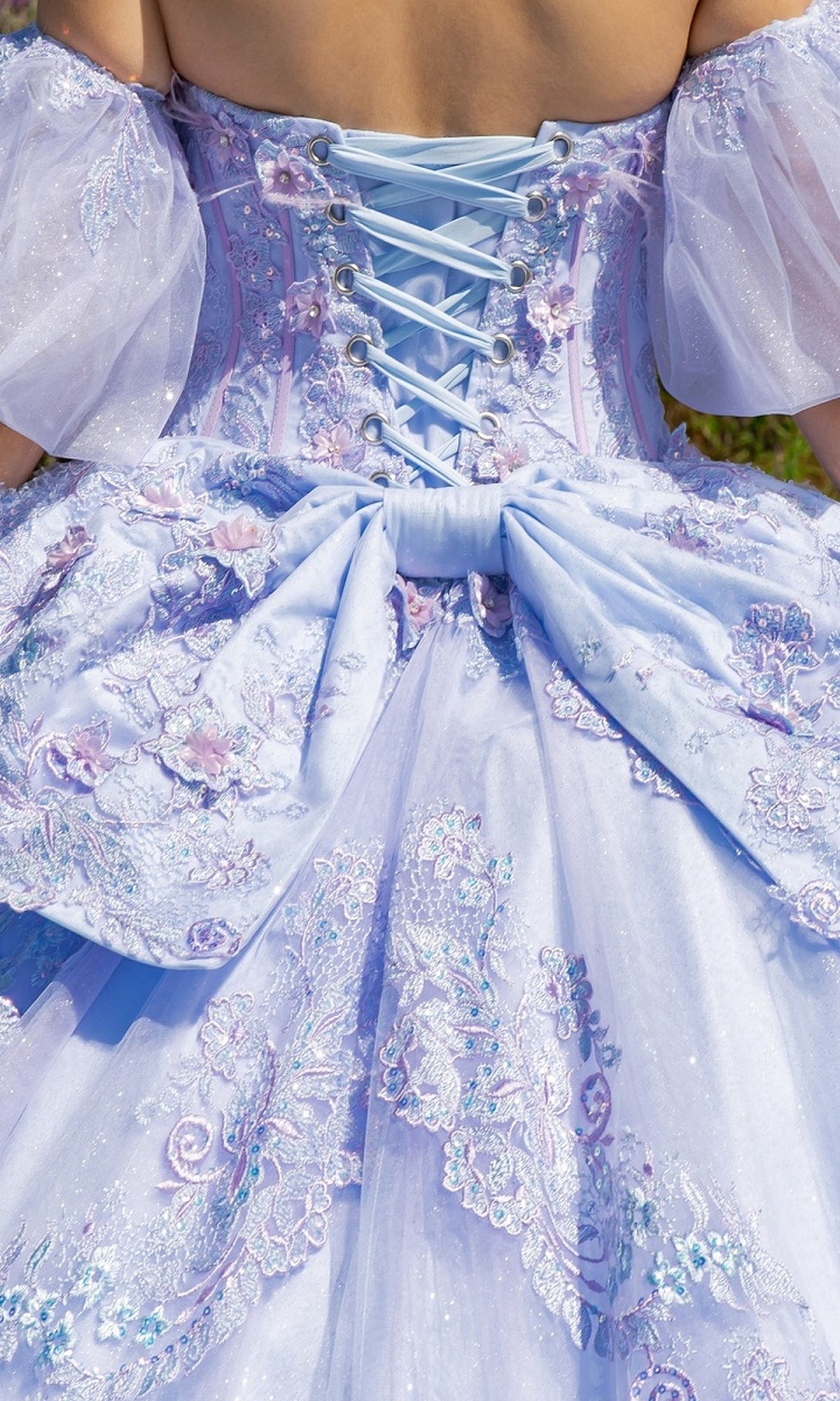 The Quinceanera Ball Gown 8115J features a close-up of the back with lace-up ribbon, floral embroidery, a large bow, and removable puff sleeves in light blue.